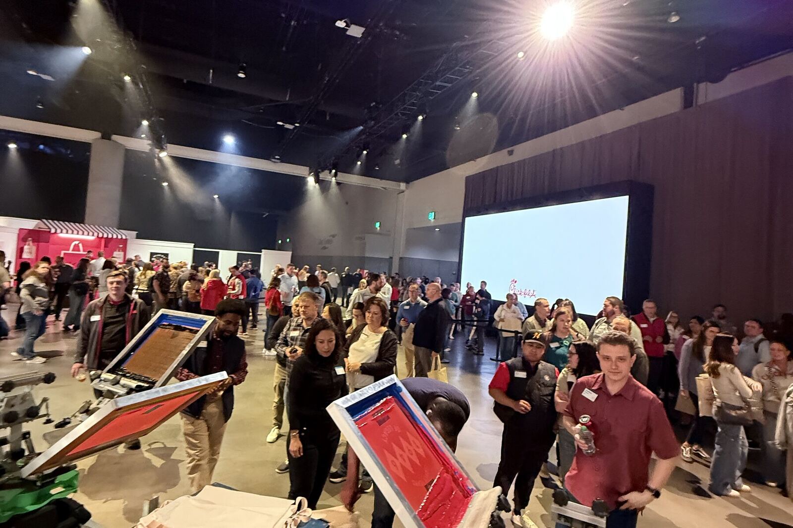 Event crew carrying screens across a busy venue floor while guests queue nearby for merch