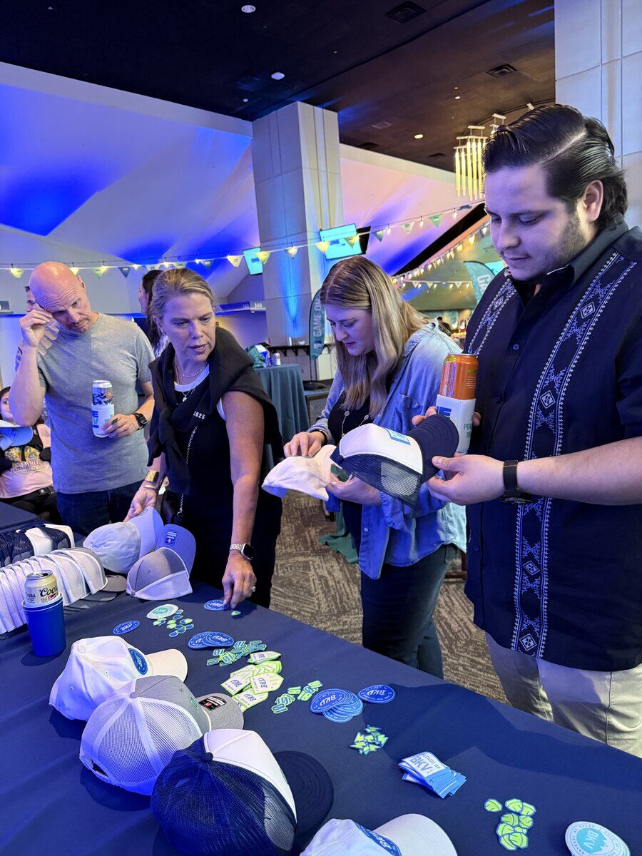 Guests choosing caps and patches from a merch table at an indoor evening event